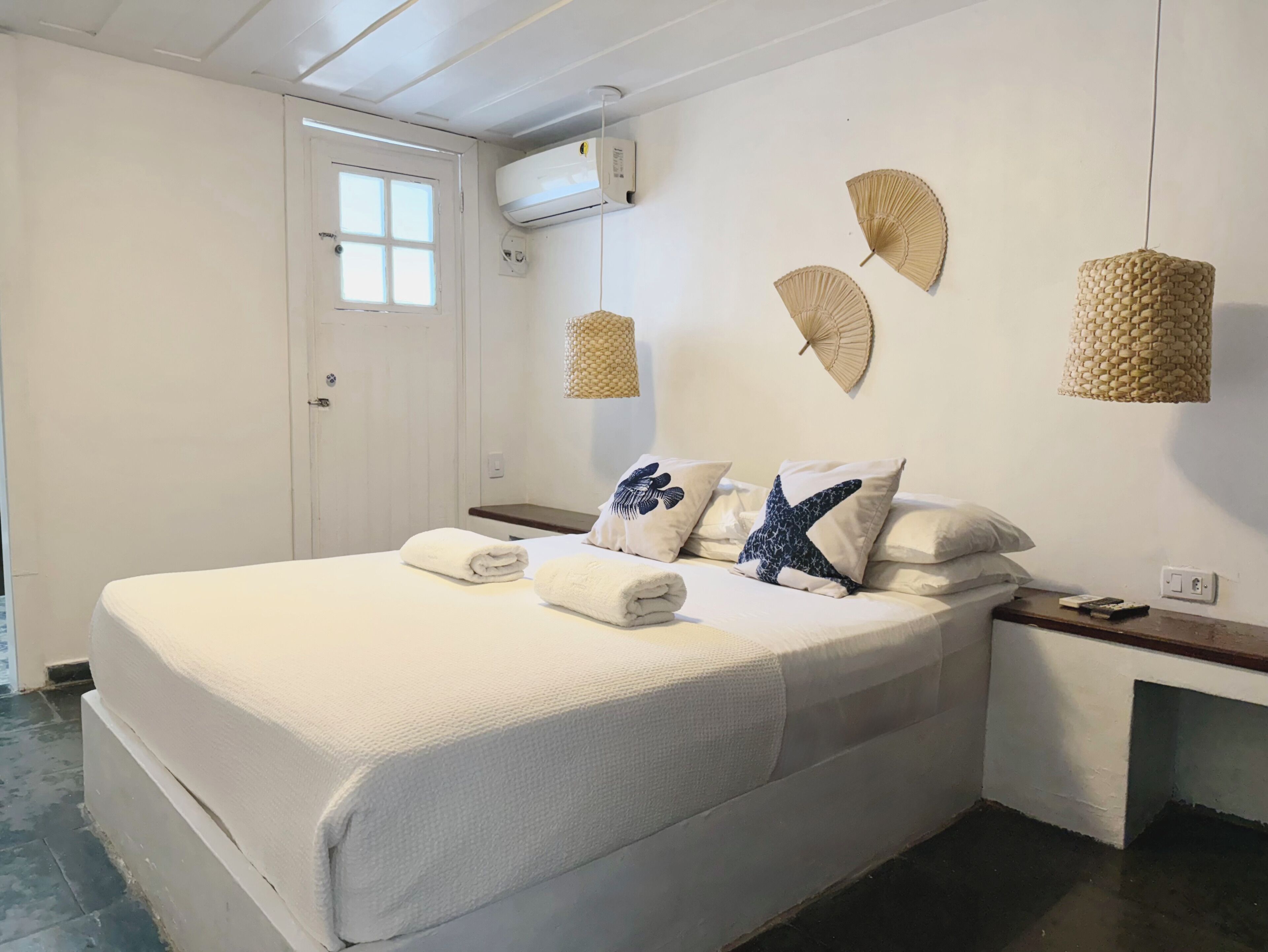 A neatly made bed with towels, a bedside table, and a wall-mounted air conditioner.