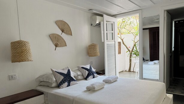 A bedroom with a bed, two wall fans, and a view of an outdoor area. -  Peixe Crew Centro (Búzios)