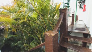 A wooden staircase with a brick handrail, surrounded by lush green palm trees. -  Peixe Crew Centro (Búzios)