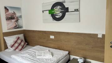 A hotel room with a bed, a wooden headboard, a wall-mounted painting, a nightstand, and a bedside table.