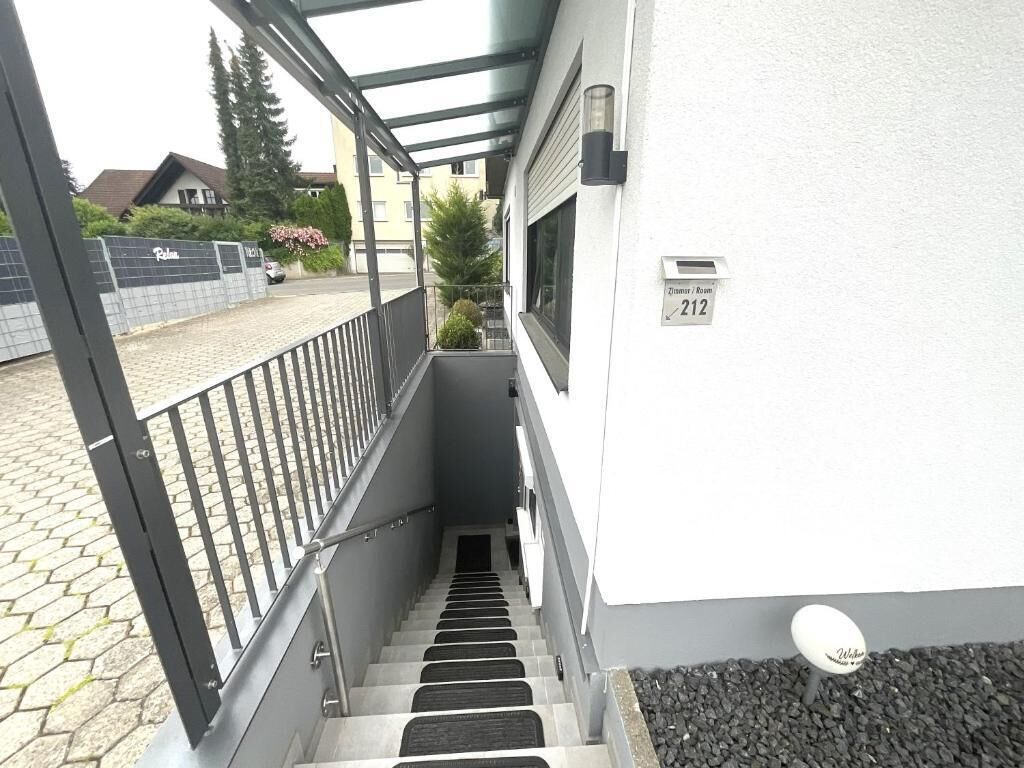 Una escalera estrecha conduce a un balcón con barandilla de metal. Un buzón con el número 212 está sujeto a la pared.