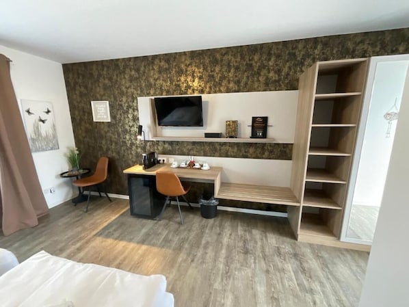 A modern hotel room with a flat-screen TV mounted on the wall, a desk with a chair, a bed, and a built-in wardrobe. - Gästehaus Würzburg 24h (Estenfeld)