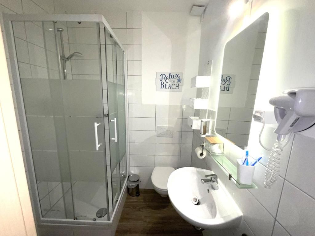 A modern bathroom with a glass-enclosed shower, a white sink, a toilet, and a mirror with a telephone.