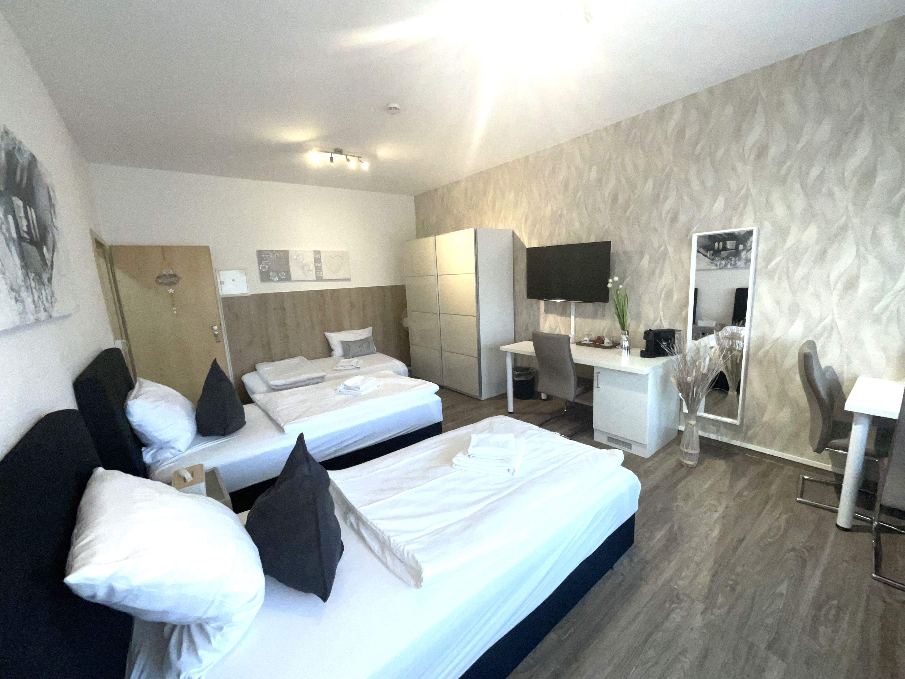 A hotel room with two beds, a desk, a chair, a TV, and a wardrobe.