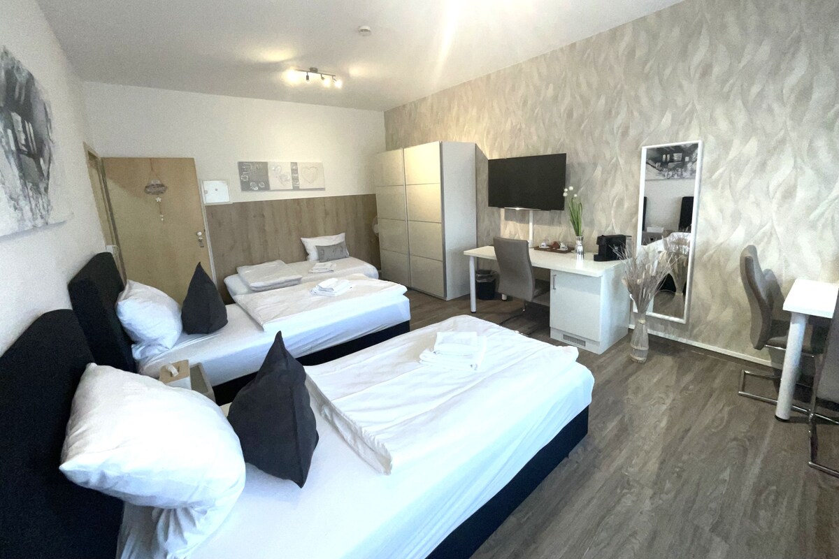 A hotel room with two beds, a desk, a chair, a TV, and a wardrobe.