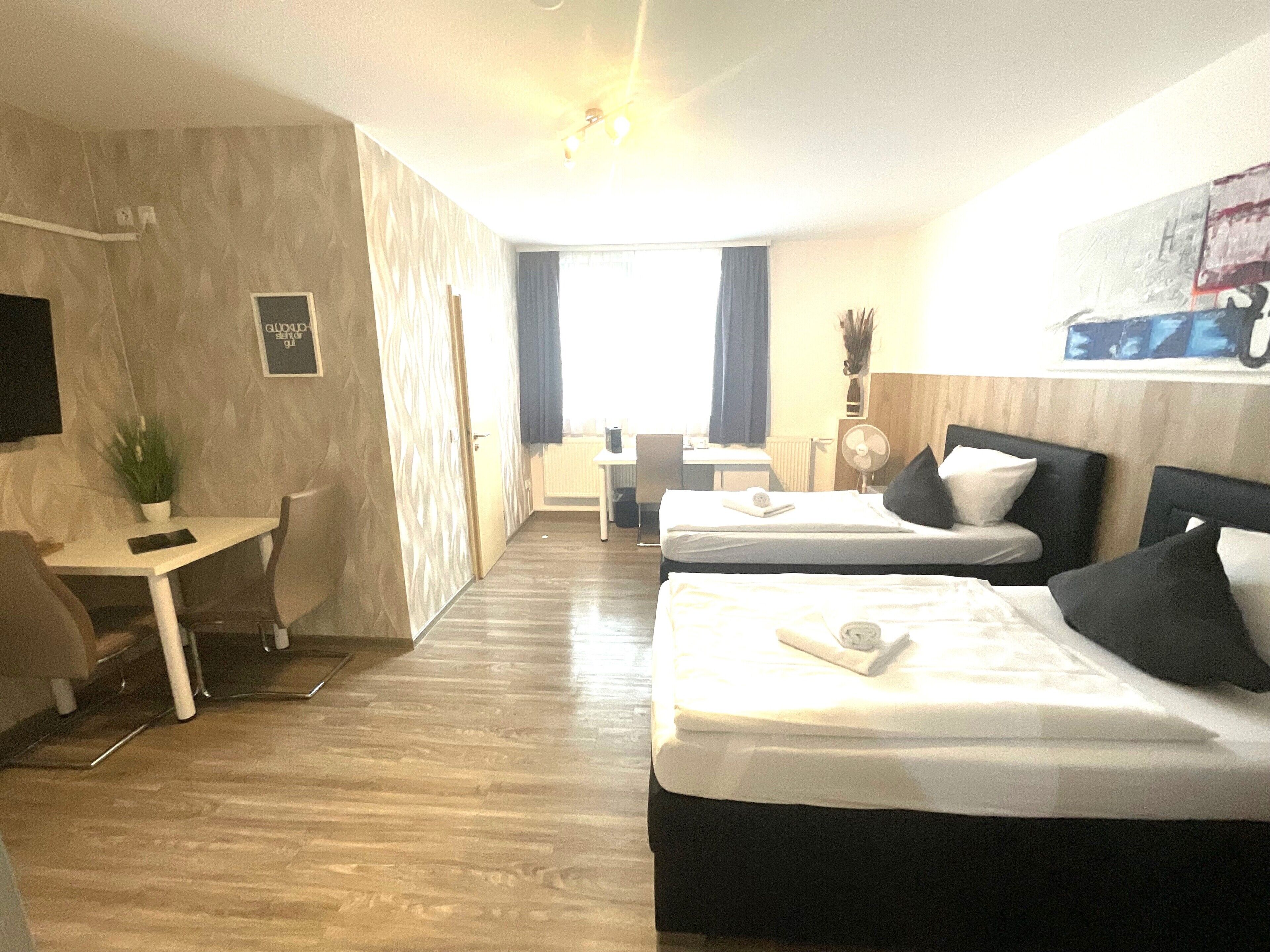 Hotelkamer met twee bedden, een bureau, een stoel, een televisie en een raam met gordijnen.