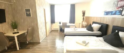 A hotel room with two beds, a desk, a chair, a TV, and a window with curtains.