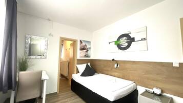 A hotel room with a bed, bedside table, chair, and a desk.