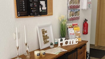 A wooden reception desk with a framed welcome sign, a fire extinguisher, and informational posters on the wall.