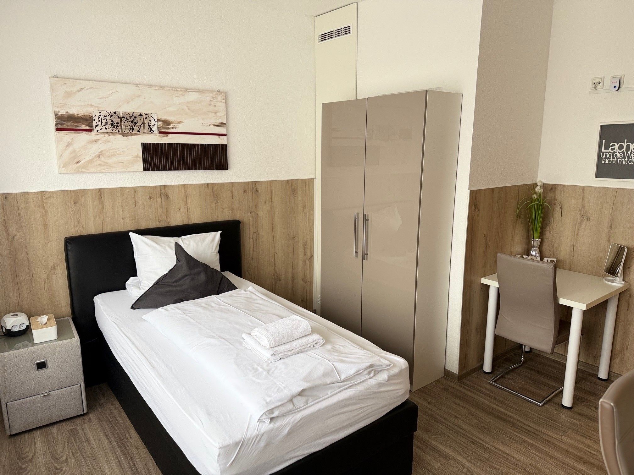 Habitación de hotel con cama, mesita de noche, armario y un pequeño escritorio con silla.