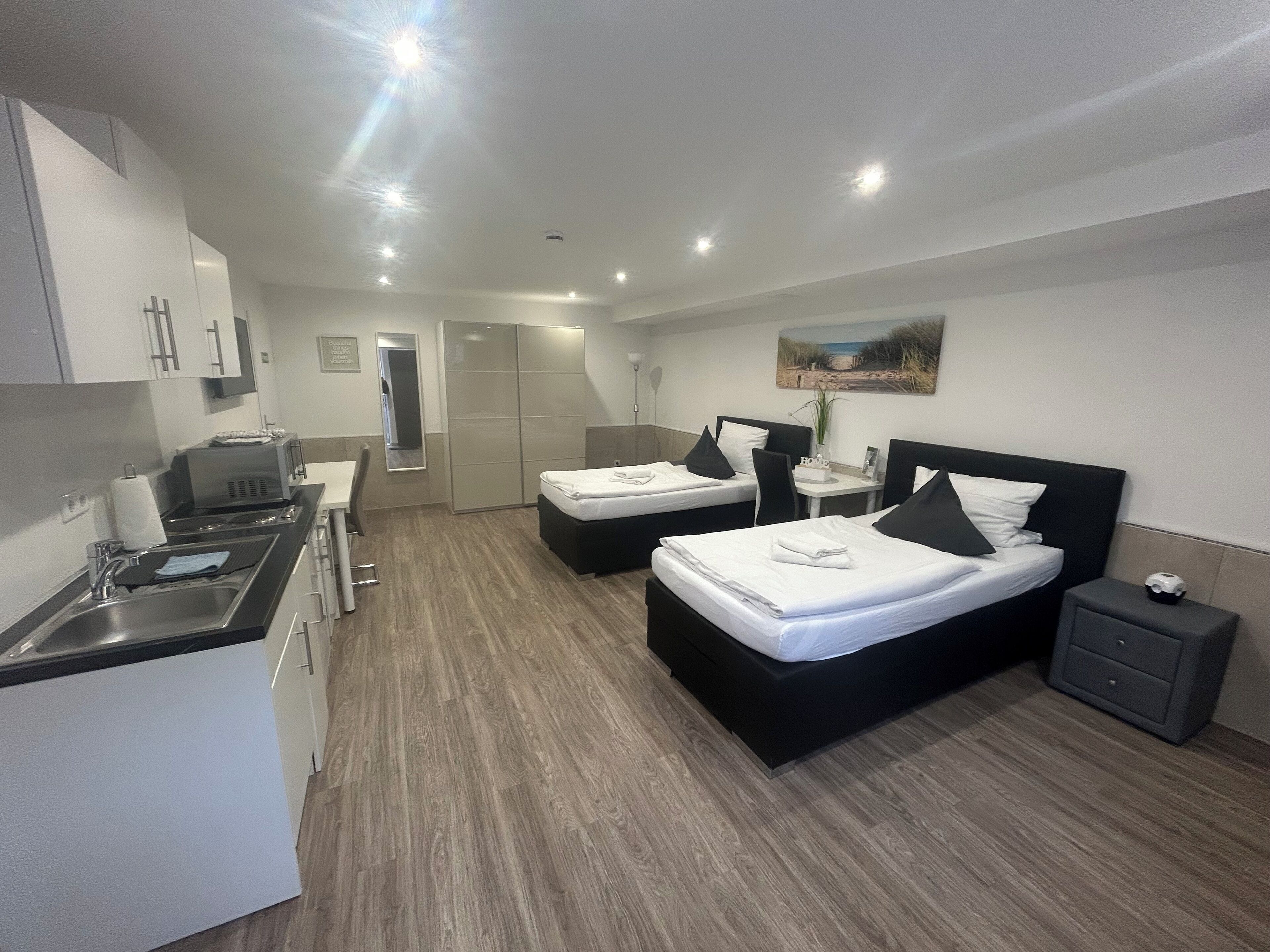 A modern hotel room with two beds, a kitchenette, a bathroom, and a small dining area.