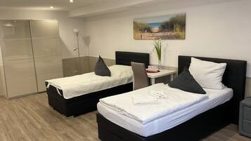 Habitación de hotel con dos camas, un escritorio con silla, un cuadro en la pared y un armario con puerta corredera.