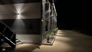 A modern building with a metal facade, a staircase, and small plants along the walkway. - Gästehaus Würzburg 24h (Estenfeld)