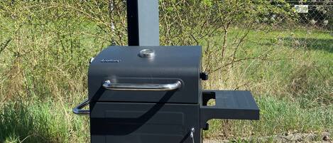A portable grill with a storage compartment containing bags of charcoal and a bag of wood.