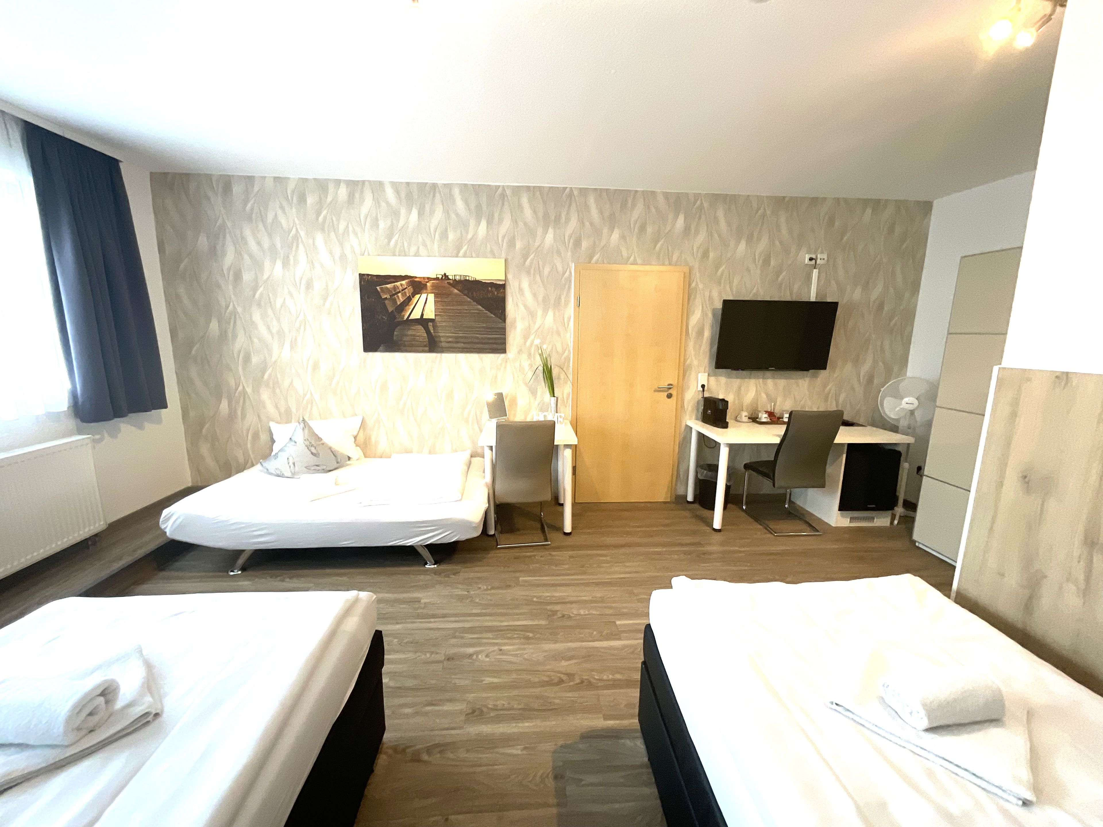 Habitación de hotel con dos camas, un escritorio, una silla, un televisor y una puerta.