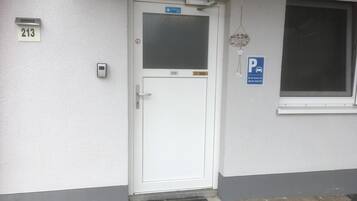 Puerta blanca con una placa que indica el número '213', un letrero de 'Bienvenido' y un letrero de 'Estacionamiento' que señala un lugar reservado para la habitación '213'.