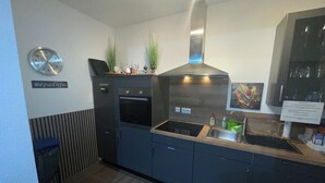 A modern kitchen with a built-in oven, a stainless steel range hood, a sink, and a clock on the wall. - Gästehaus Würzburg 24h (Estenfeld)