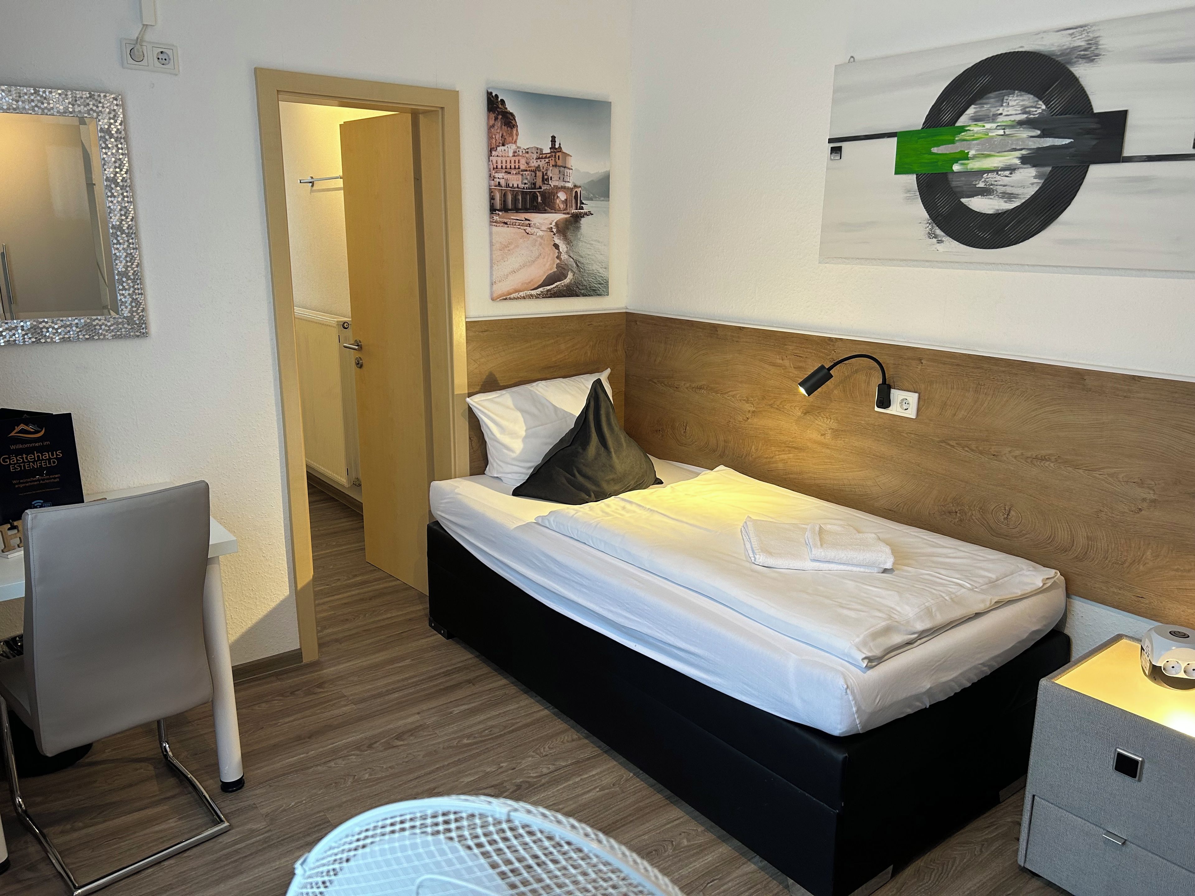 Ein Hotelzimmer mit einem Bett, einem Schreibtisch, einem Stuhl, einem Nachttisch und einer Wand mit einem Gemälde.