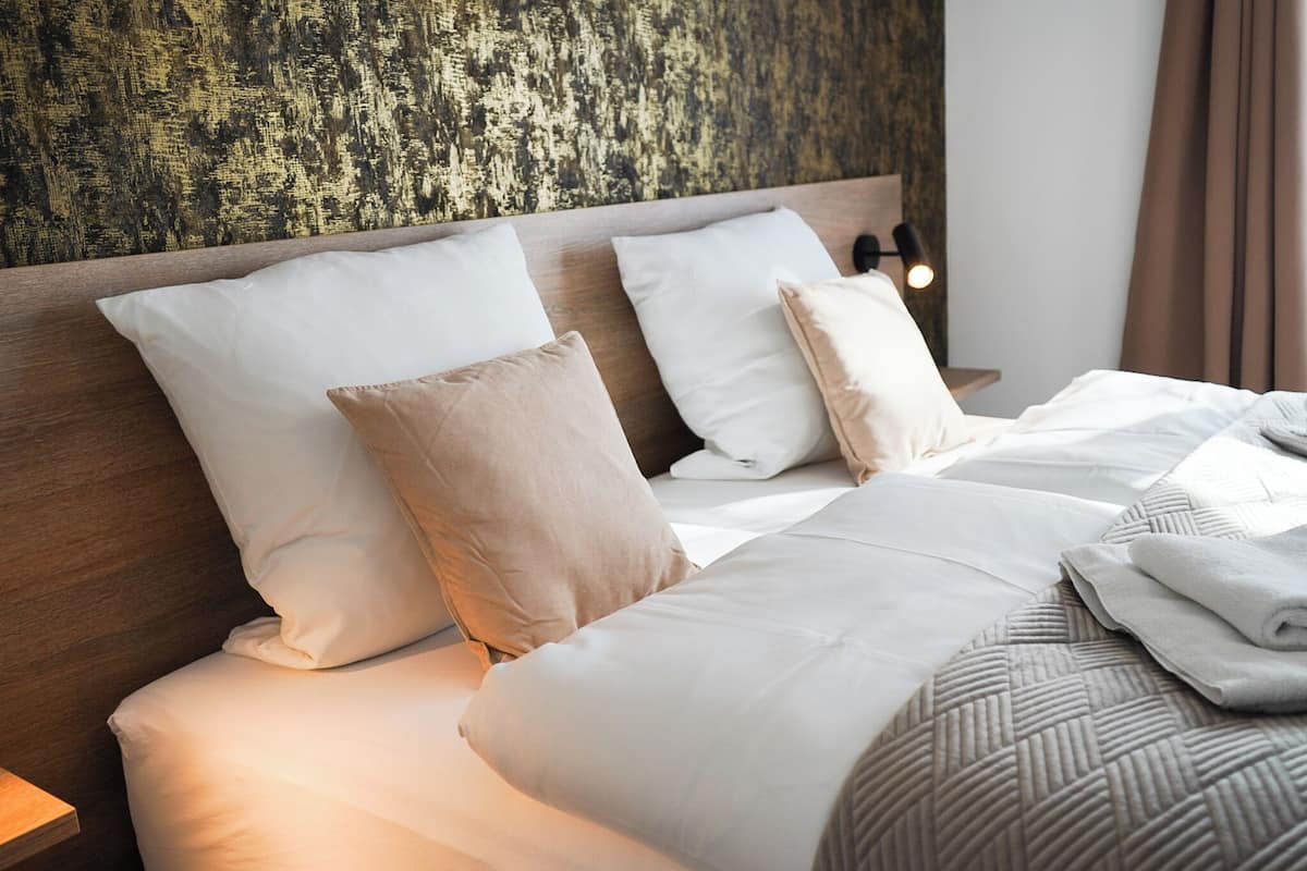 Un lit bien fait, avec des oreillers blancs et beige, une tête de lit en bois et un mur texturé derrière.