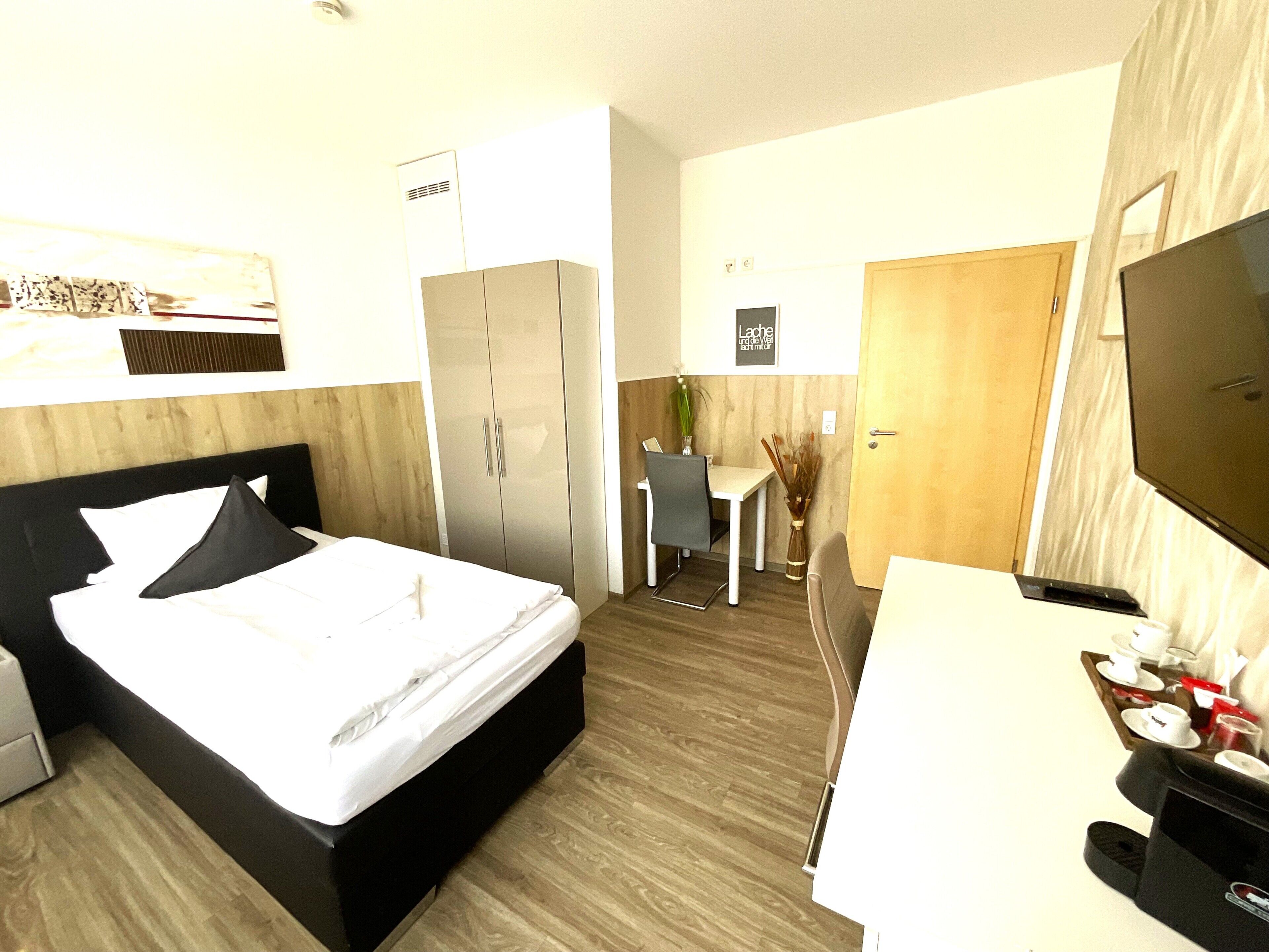 A hotel room with a bed, a desk, a chair, a TV, and a wardrobe.