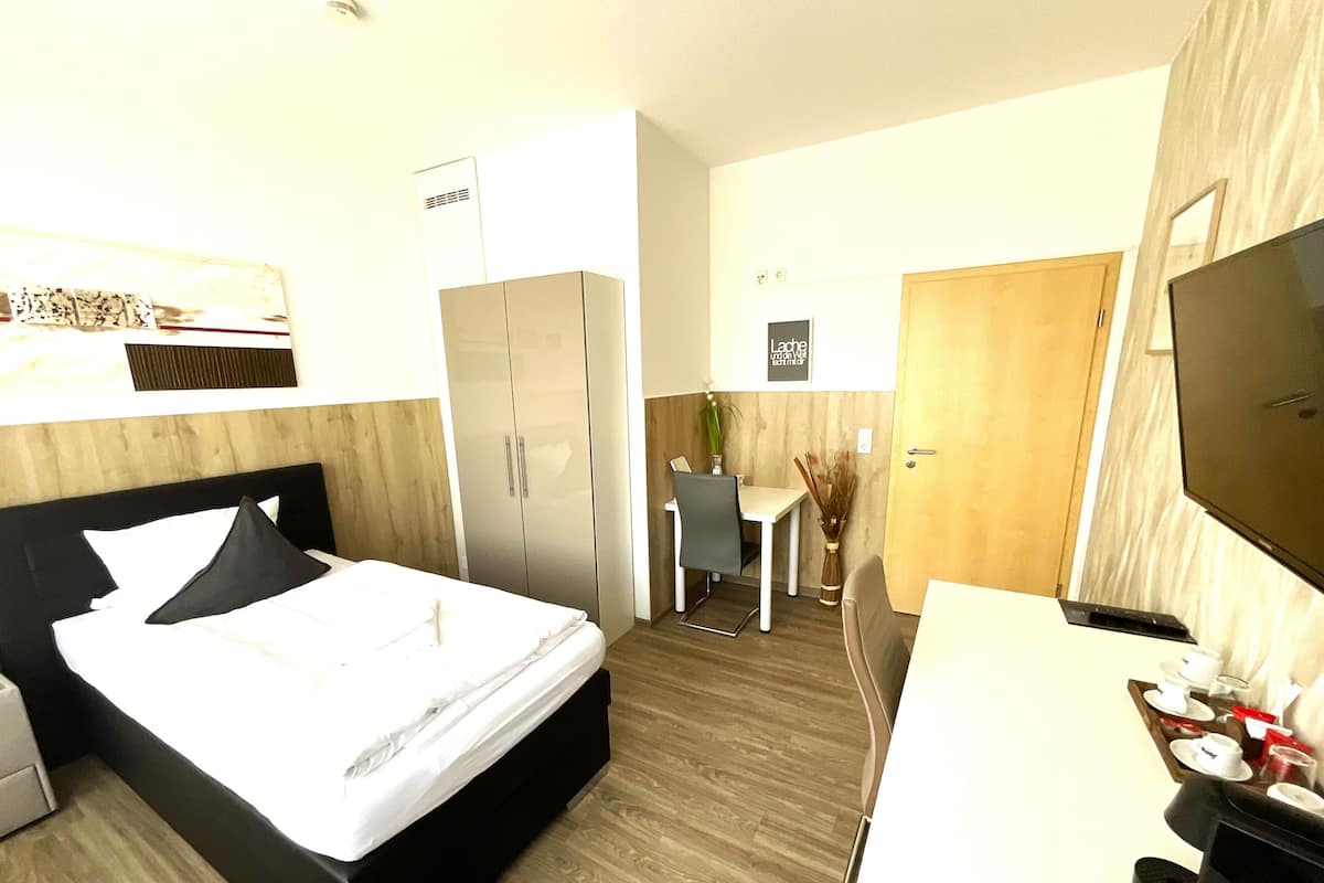 Une chambre d’hôtel comprenant un lit, un bureau avec une télévision, une armoire et une petite table avec une chaise.