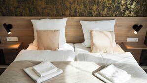 A double bed with two pillows, a folded towel, and a headboard with wall-mounted lights. - Gästehaus Würzburg 24h (Estenfeld)