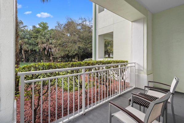A balcony with a white railing, a bench, and a view of a landscaped garden with trees and shrubs.