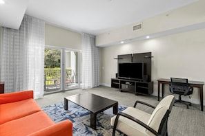 A modern living room with a flat-screen TV, a sofa, a coffee table, and a desk with a chair.