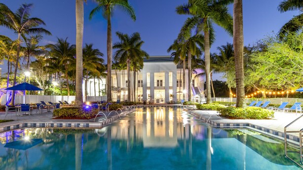 A pool area with lounge chairs, palm trees, and a building with columns. - 3 Bedroom/4 Bath Townhouse, Pool, Parking, & More! (Miami)