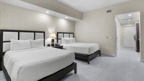 A hotel room with two beds, a nightstand with a lamp, and a door leading to a hallway. - Paradise Retreat | King Suite w/ Kitchen (Miami)