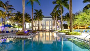 A swimming pool with lounge chairs and palm trees, surrounded by a building with large windows. - Paradise Retreat | King Suite w/ Kitchen (Miami)