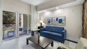 Un salon moderne avec un canapé bleu, une table basse et une lampe. Il y a un balcon avec vue sur les arbres et une rambarde.