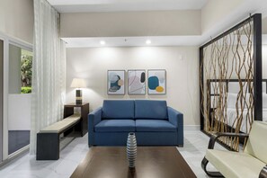 A modern living room with a blue sofa, a coffee table with a vase, a bench, and a decorative screen.