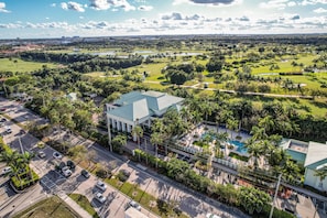 An aerial view of a resort with a large building, a swimming pool, and surrounding greenery.