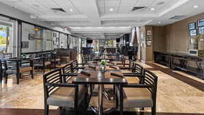 Een ruim restaurant met meerdere tafels en stoelen, een modern plafondontwerp en afbeeldingen in lijsten aan de muren.