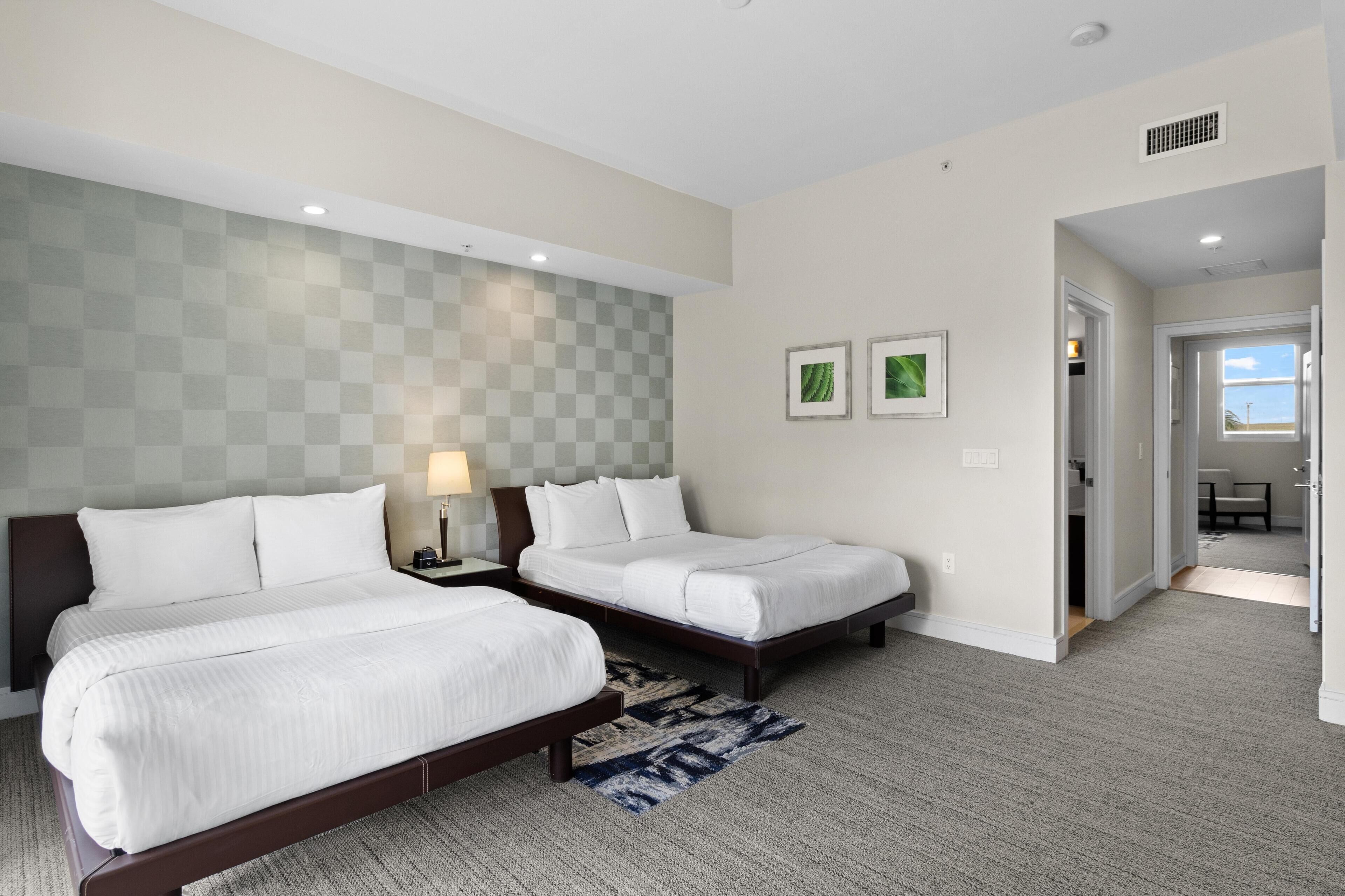A hotel room with two beds, a checkered wall, and a view of the outside.