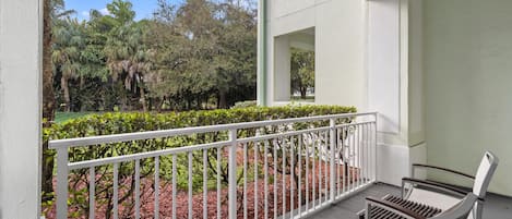 A balcony with a white railing, a bench, and a view of a landscaped garden with trees and shrubs.