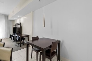 Un espace repas moderne avec une table et des chaises en bois foncé, un téléviseur et un luminaire suspendu.