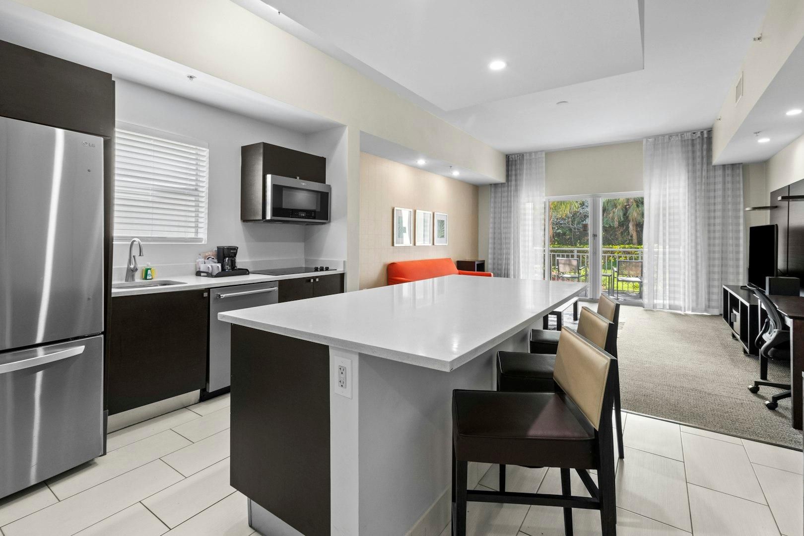 A modern kitchen with a central island, stainless steel appliances, and a dining area with a view.