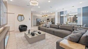 A modern living room with a grey sectional sofa, a glass coffee table, and a black armchair. - 12BR house with private pool in Paradiso Grande (Orlando)