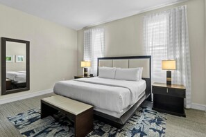 Habitación de hotel con una cama grande, dos mesitas de noche con lámparas, un banco y un espejo grande en la pared.