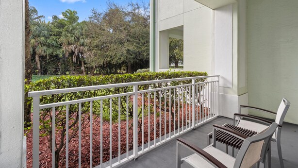 A balcony with a white railing, a bench, and a view of a landscaped garden with trees and shrubs. - King Studio Oasis | Room to Relax (Miami)
