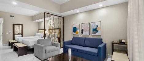 A modern hotel room with a bed, a sofa, a coffee table, and artwork on the wall.
