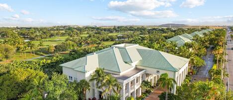Un edificio grande con techo verde, rodeado de abundante vegetación y un campo de golf.