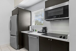 Una cocina moderna con un refrigerador de acero inoxidable, un microondas integrado y una encimera negra.