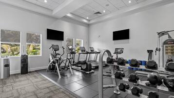 Un gimnasio con equipo de ejercicio, un dispensador de agua y un ventanal con vista a zonas verdes.