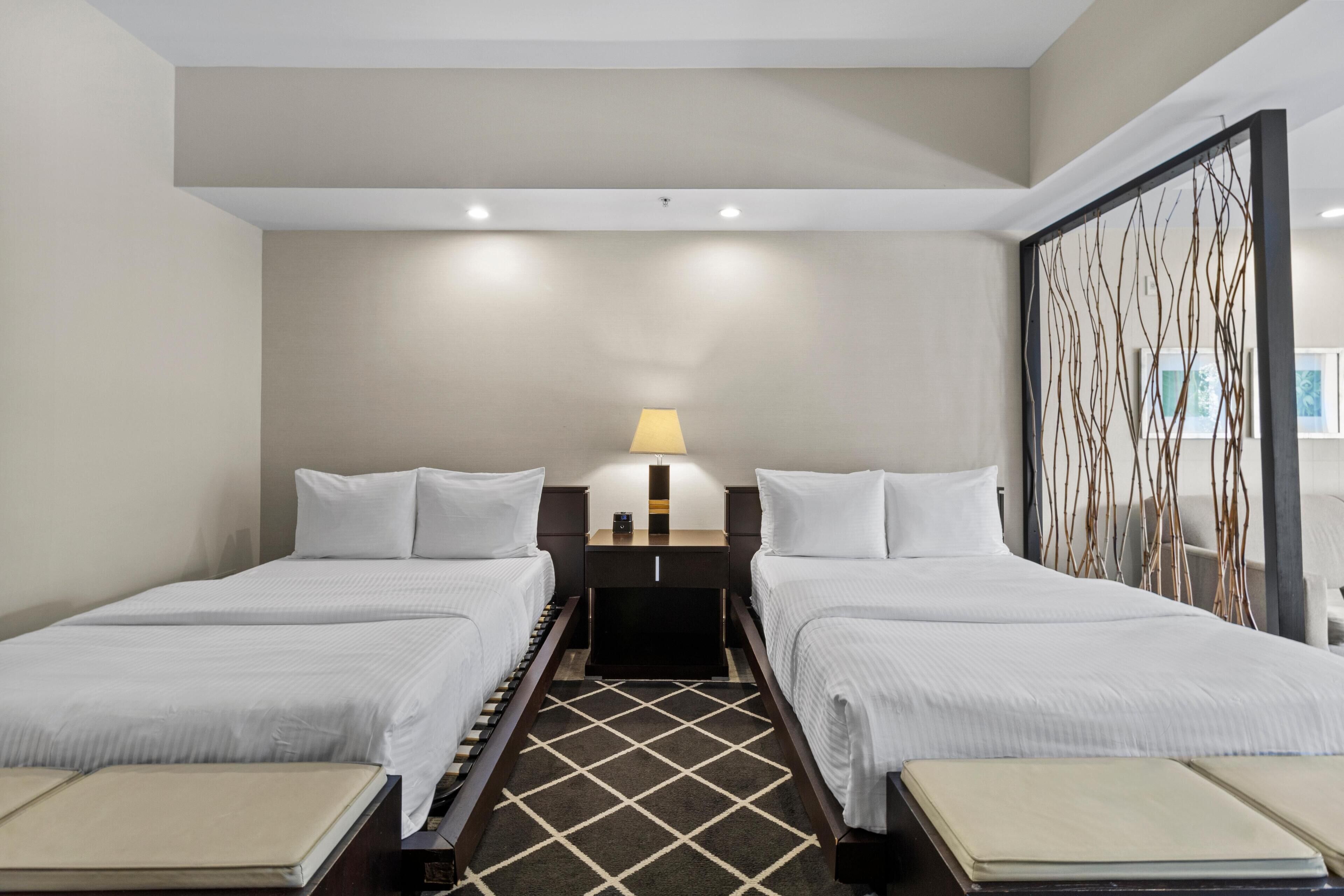 A hotel room with two single beds, a small desk, a lamp, and a decorative wall panel.