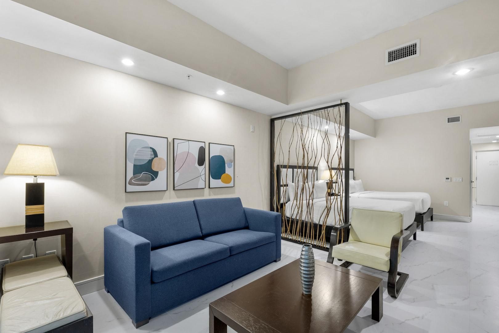 A hotel room with a blue sofa, a small table, a bed, and a decorative screen.
