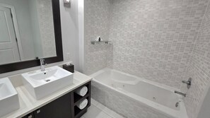 Features a sleek, white-tiled design with a large bathtub and matching vanity area.