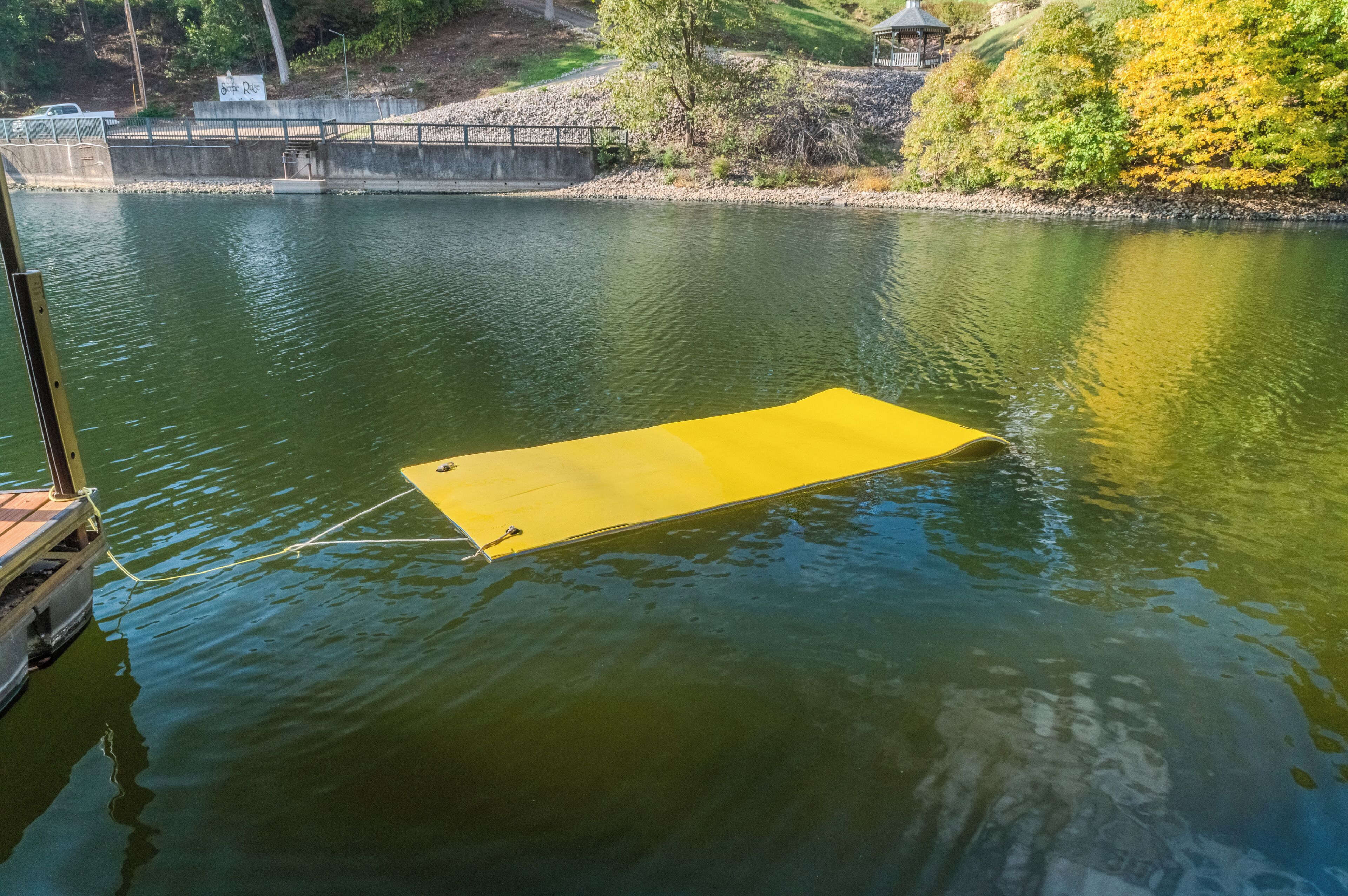 Una piattaforma galleggiante gialla su un'area d'acqua, circondata da vegetazione e un ponte sullo sfondo.